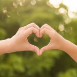 Mother and her child holding hands in heart shape framing on nature background